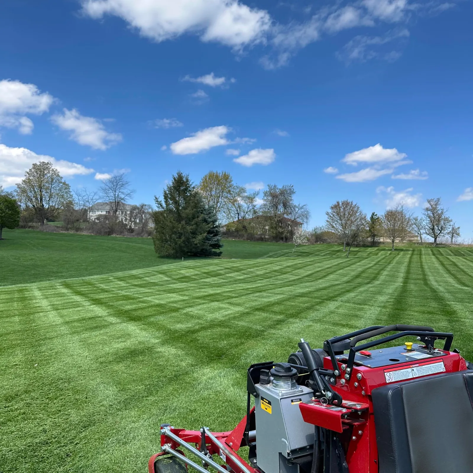 A freshly striped lawn on a large property, with a red stand-on mower in the foreground