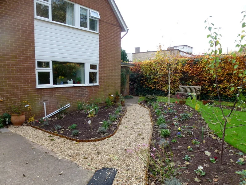 The same side of the house with a gravel path between new edged planting beds